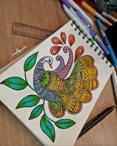 a drawing of a colorful bird on top of a wooden table next to markers and pencils