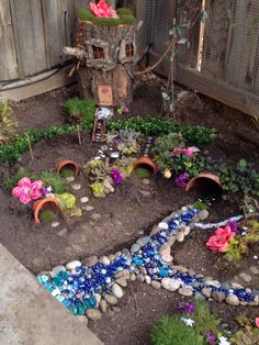 a garden with flowers and rocks in the ground next to a tree stump that has been made into a fairy house