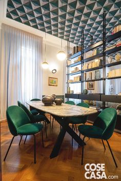 a dining room table with green chairs and bookshelves in the backround