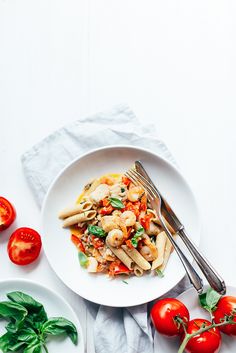 a white plate topped with pasta and vegetables next to two plates of tomatoes, spinach