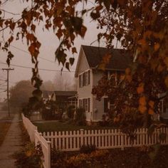 a white picket fence sitting in front of a house on a foggy day with houses behind it