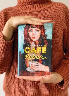 a woman holding up a book about cafe eden in front of her face and hands