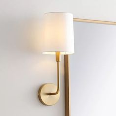 a wall light with a white shade on it's side next to a mirror