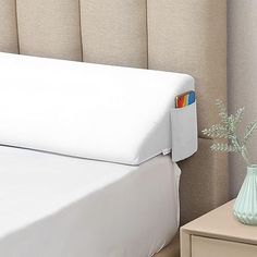 a bed with a white headboard next to a small table and vase on it