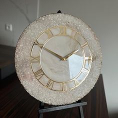 a white clock with gold trim on top of a wooden table