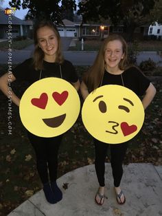 two girls in black shirts are holding yellow emotictive smiley faces with hearts on them