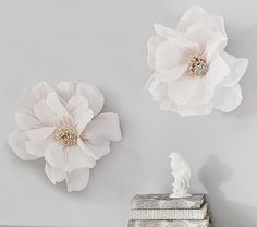 three white flowers are hanging on the wall next to two silver boxes and a figurine