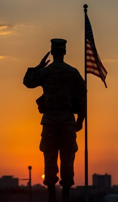 the silhouette of a soldier saluting at sunset with an american flag in the foreground