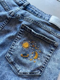 a pair of blue jeans with embroidered stars and the moon on them, sitting on a white surface