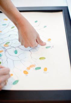 a person is drawing on a white paper with colored leaves in the shape of a tree