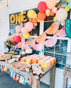 a table filled with lots of food and balloons on the side of a white house