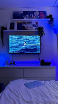 a flat screen tv sitting on top of a white dresser next to a blue light