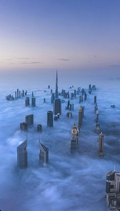 an aerial view of skyscrapers surrounded by clouds in the middle of the city at dusk