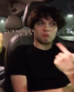 a young man sitting in the back seat of a car pointing at something with his finger