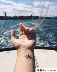 a person's hand with a compass tattoo on their left wrist and the ocean in the background