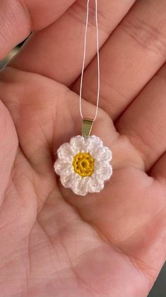 a hand holding a small crocheted flower on a white string with yellow center