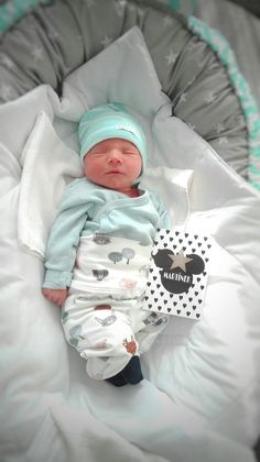 a baby laying on top of a bed wearing a blue hat and diaper next to a tag