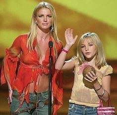 two women standing next to each other at a awards show, one holding a doughnut and the other raising her hand