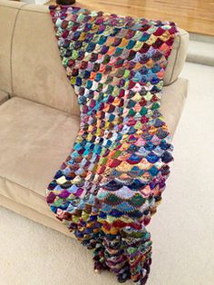 a crocheted blanket sitting on top of a couch next to a white chair