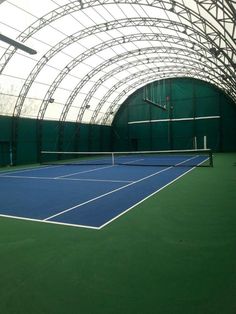 an indoor tennis court with green walls and white lines on the floor, surrounded by arches