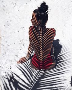 a woman sitting on the ground with her back turned to the camera, casting a shadow