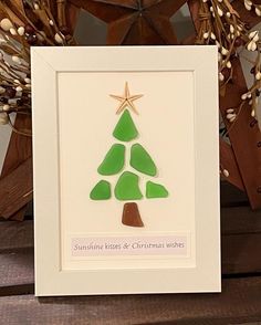 a christmas card with a green tree and star on it, sitting next to some branches