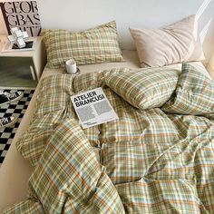 a bed covered in plaid sheets and pillows with a book on top of the comforter