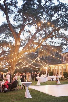 an outdoor wedding reception under a large tree with lights strung from the branches and hanging lanterns