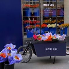 a bicycle parked next to a flower shop with flowers in the window and bags on the front