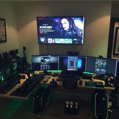 there are many computer monitors on the desk with green lights in front of them and a large screen behind them