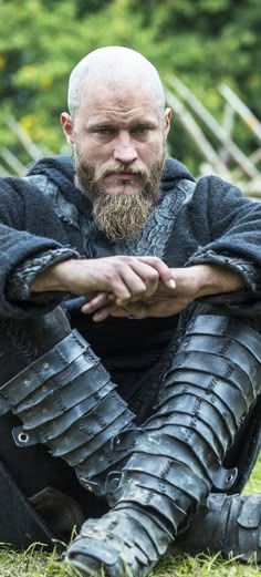 a man in armor sitting on the ground with his arms crossed and looking at the camera