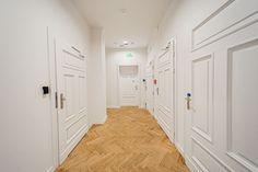 an empty hallway with white walls and wooden floors is pictured in this image, there are several doors on either side of the hall