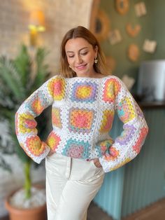 a woman wearing a colorful crochet sweater and white pants