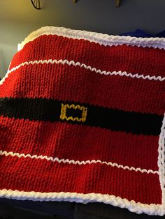 a red and black knitted blanket with a gold buckle on the front, sitting on a bed