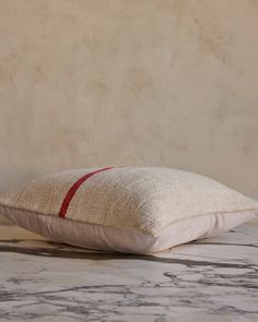 a white pillow sitting on top of a marble floor next to a beige and red wall