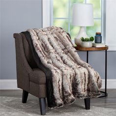 a chair with a blanket on it next to a table and lamp in front of a window