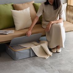 a woman sitting on a couch next to some pillows and an open laptop computer case