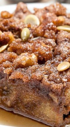 a square piece of cake with nuts on top sitting on a white plate, ready to be eaten