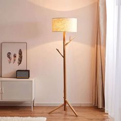 a wooden floor lamp with a white shade on it in a living room next to a dresser