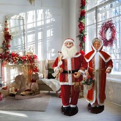 two santa clause statues standing in front of a christmas tree