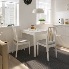 a white table with two chairs and a clock on the wall in a kitchen area