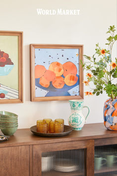 two paintings on the wall above a wooden table with plates and bowls in front of it