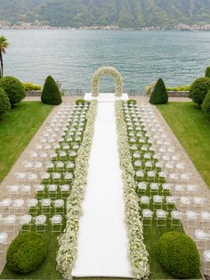 an outdoor ceremony set up with white flowers and greenery on the lawn next to water