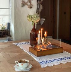 two candles are lit on a table with a tea cup and saucer