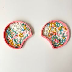 two pink plates with designs on them sitting next to each other in front of a white background