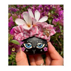 a hand holding up a rock with a flower on it and an image of a cat's face painted on it