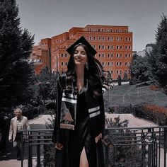 a woman wearing a graduation cap and gown standing in front of a fenced area