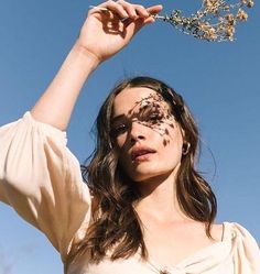 a woman is holding her hair in the air with flowers on her face and branches behind her