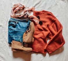 an orange sweater, jeans and boots are laid out on a white sheeted surface