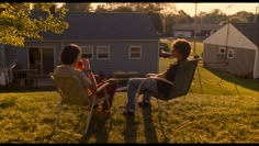 two women sitting in lawn chairs talking to each other on the grass near a house